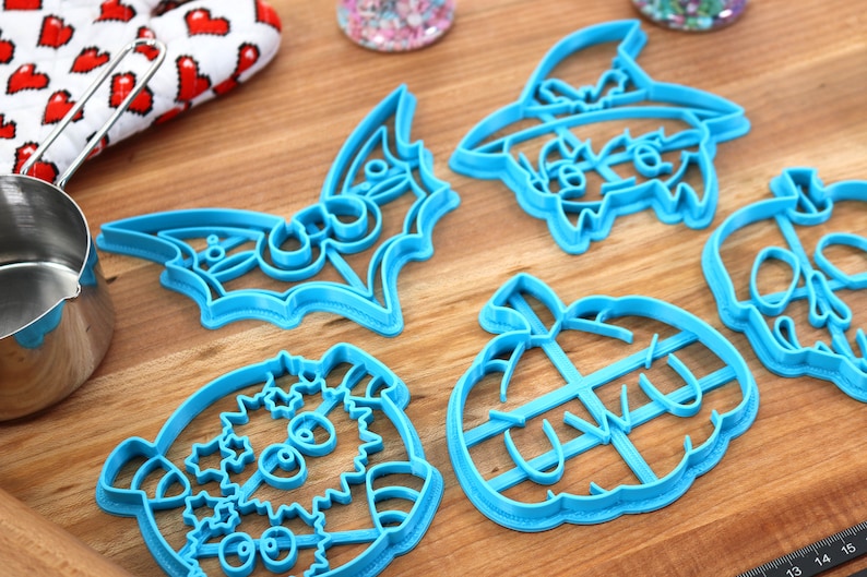 May include: A set of six blue plastic Halloween cookie cutters. The cutters are shaped like a bat, a pumpkin, a ghost, a skull, a witch, and a monster.
