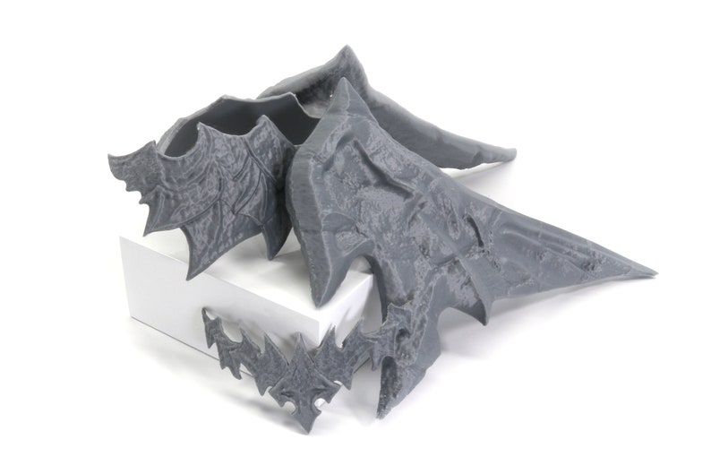 May include: Four grey 3D printed wings with intricate details. The wings are arranged in a pile on a white surface.