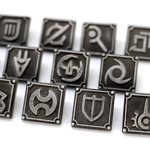 May include: Close-up of several square, silver-colored metal pins with various symbols. Each pin has a raised border and a unique design in the center. The pins are arranged on a white surface.