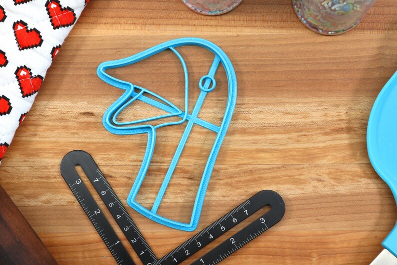 May include: A blue plastic cookie cutter shaped like a goose head. The cutter is on a wooden surface.