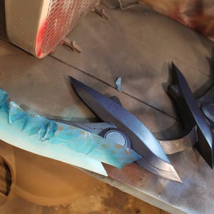 May include: A blue and black prop weapon with a blue and white paint job. The weapon is made of plastic and has a sharp, pointed tip.