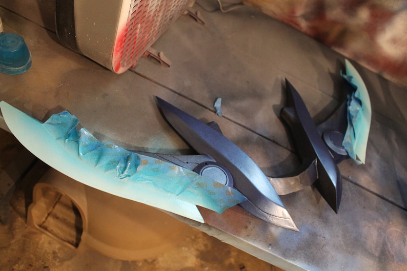 May include: A blue and black prop weapon with a blue and white paint job. The weapon is made of plastic and has a sharp, pointed tip.