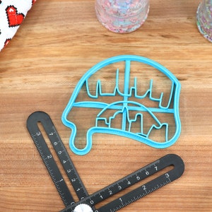 May include: A light blue plastic cookie cutter shaped like a dripping ice cream cone with a city skyline design.