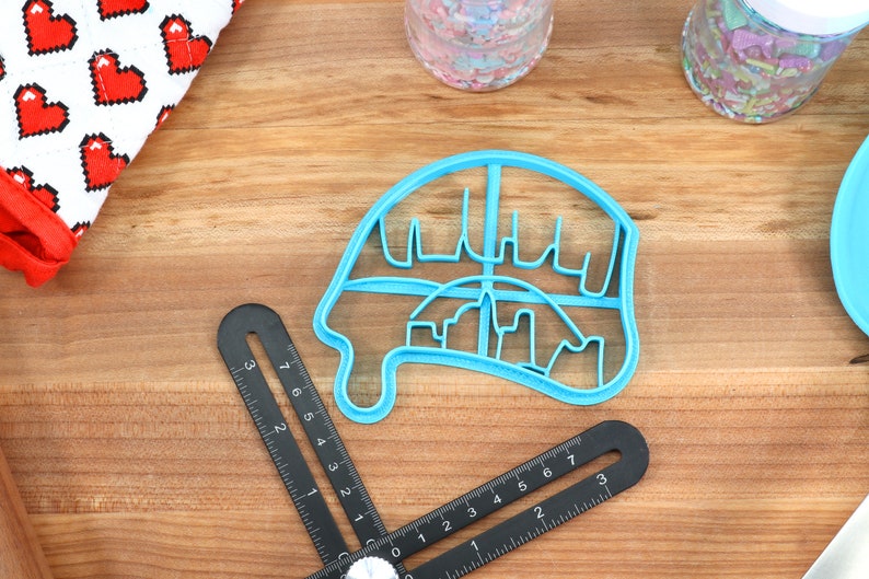 May include: A light blue plastic cookie cutter shaped like a dripping ice cream cone with a city skyline design.