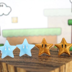 May include: A pair of earrings featuring two blue and two gold star-shaped charms. The stars have a black outline and a raised design.