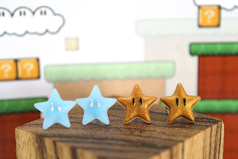 May include: A pair of earrings featuring two blue and two gold star-shaped charms. The stars have a black outline and a raised design.