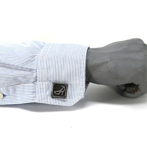 May include: A blue and white striped dress shirt with a silver cufflink featuring a stylized shoe design.