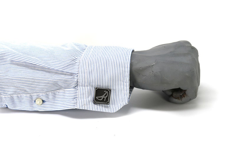 May include: A blue and white striped dress shirt with a silver cufflink featuring a stylized shoe design.