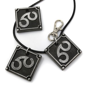 May include: Three silver-colored pendants with a black background and a stylized symbol. The pendants are attached to a black cord and a silver clasp.