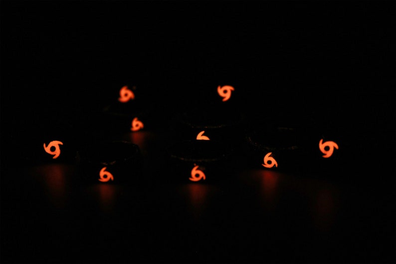 May include: A group of nine black silicone rings with a glow-in-the-dark orange swirl design.