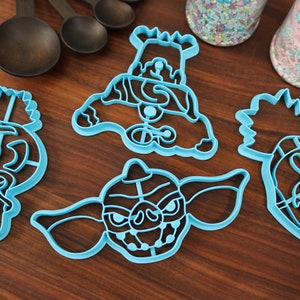May include: Set of four blue plastic cookie cutters shaped like different characters from the movie Gremlins. The cutters are on a wooden surface.