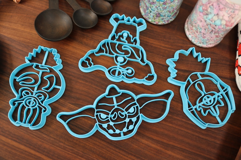 May include: Set of four blue plastic cookie cutters shaped like different characters from the movie Gremlins. The cutters are on a wooden surface.