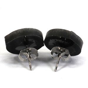 May include: A pair of black stud earrings with silver posts. The earrings are round and have a smooth, matte finish.