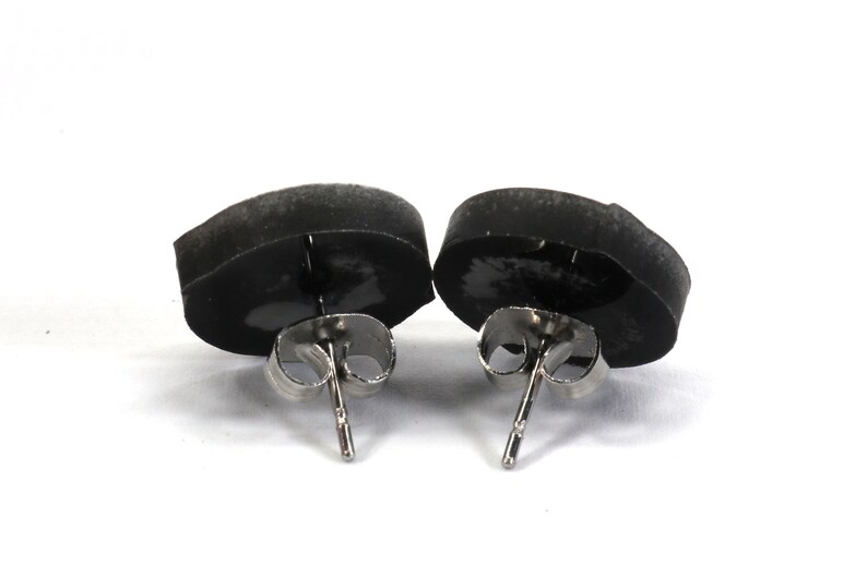 May include: A pair of black stud earrings with silver posts. The earrings are round and have a smooth, matte finish.