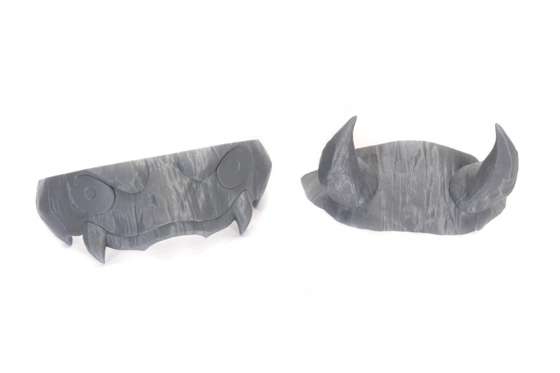 May include: Two gray plastic Halloween costume pieces. One piece is a pair of horns and the other is a set of fangs with eyes.