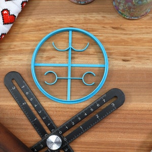 May include: A blue plastic cookie cutter shaped like a circle with four smaller circles inside. The cookie cutter is on a wooden surface.
