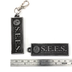 May include: Two silver metal keychains with the text "S.E.E.S. SPECIALIZED EXTRACARICULAR EXECUTION SQUAD" on them. The keychains are about 2 inches long.