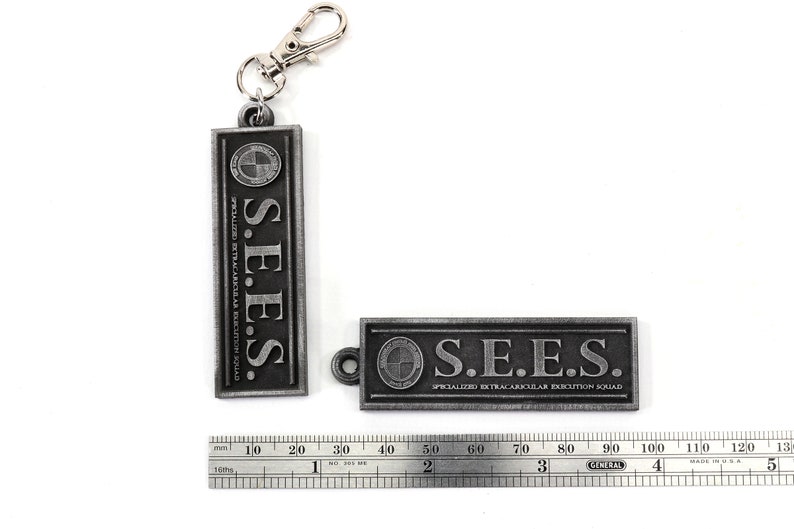 May include: Two silver metal keychains with the text "S.E.E.S. SPECIALIZED EXTRACARICULAR EXECUTION SQUAD" on them. The keychains are about 2 inches long.