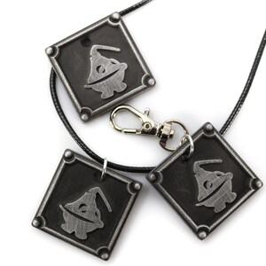 May include: Three silver-toned pendants with a black and white image of a character wearing a hat. The pendants are attached to a black cord and a silver-toned clasp.