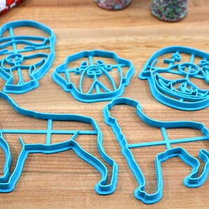 May include: Set of five blue plastic cookie cutters shaped like dogs. The cutters include a bulldog, a labrador, a pug, and two other dog breeds.