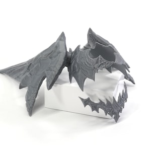 May include: A grey 3D printed dragon wing set with intricate details. The wings are separated into three pieces, with a large wing, a smaller wing, and a smaller piece that appears to be a claw or talon.