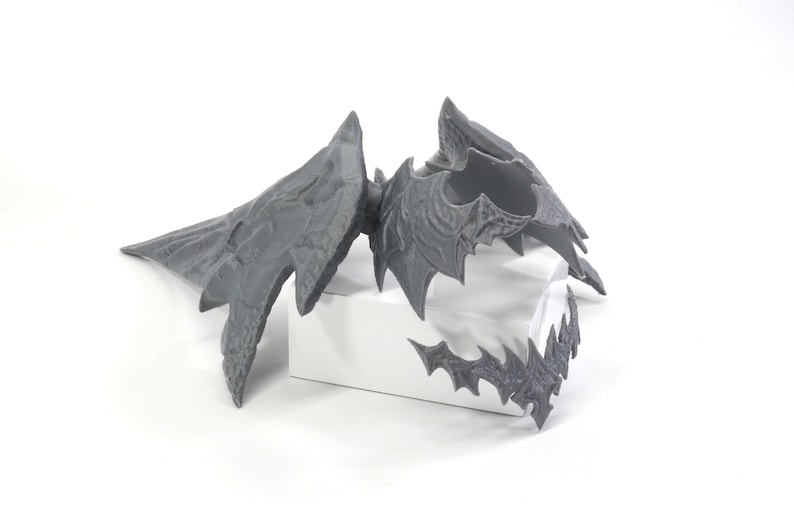 May include: A grey 3D printed dragon wing set with intricate details. The wings are separated into three pieces, with a large wing, a smaller wing, and a smaller piece that appears to be a claw or talon.