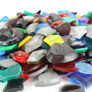 Puede incluir: Un mont&oacute;n de piezas de juego de pl&aacute;stico de colores, transl&uacute;cidas y opacas. Las piezas son de diversas formas y tama&ntilde;os, algunas con un s&iacute;mbolo o dise&ntilde;o.