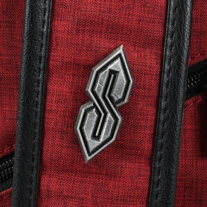 May include: Close-up of a red backpack with a textured fabric. A silver-colored emblem in the shape of a stylized "S" is affixed to the front. Black leather trim and a silver zipper are also visible.