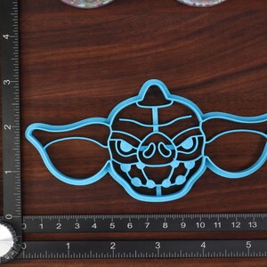 May include: A blue plastic cookie cutter shaped like the character Gizmo from the movie Gremlins. The cutter has a detailed design of Gizmo's face, including his large ears, eyes, and teeth.