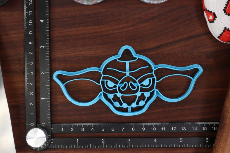 May include: A blue plastic cookie cutter shaped like the character Gizmo from the movie Gremlins. The cutter has a detailed design of Gizmo's face, including his large ears, eyes, and teeth.
