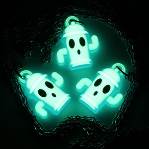 May include: Three glow-in-the-dark green and white ghost-shaped charms on a black chain necklace. The charms are shaped like fire hydrants with arms and legs.