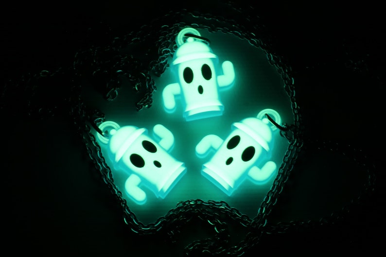 May include: Three glow-in-the-dark green and white ghost-shaped charms on a black chain necklace. The charms are shaped like fire hydrants with arms and legs.