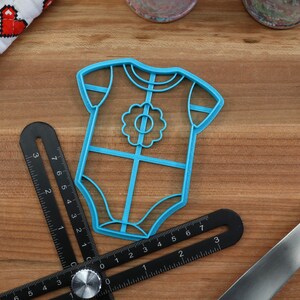 May include: Blue plastic cookie cutter shaped like a baby onesie with a flower design on the front.