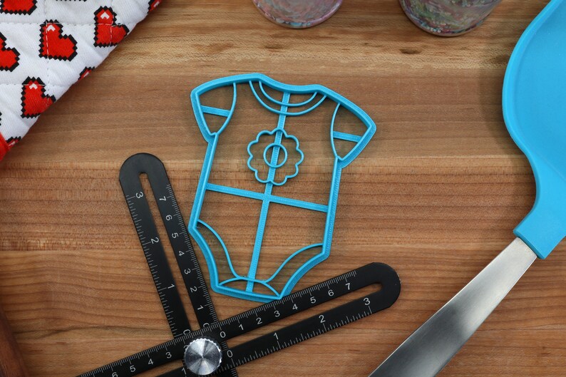 May include: Blue plastic cookie cutter shaped like a baby onesie with a flower design on the front.