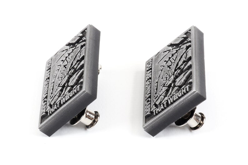 May include: Two silver-coloured pins with a cracked, textured surface. The text on the pins reads "YOU ARE GONNA CARRY THAT WEIGHT".