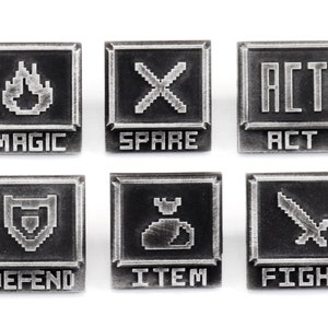 May include: Six silver-colored metal pins with pixelated graphics and text. The pins feature the words "MAGIC", "SPARE", "ACT", "DEFEND", "ITEM", and "FIGHT".