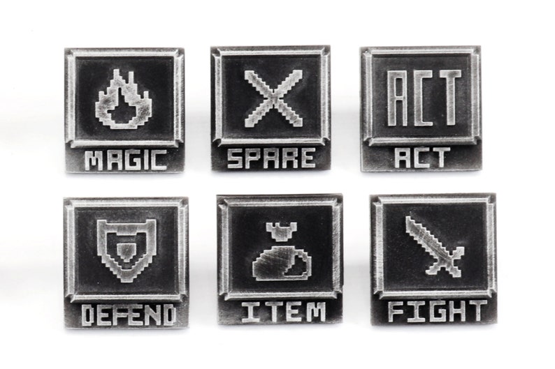 May include: Six silver-colored metal pins with pixelated graphics and text. The pins feature the words "MAGIC", "SPARE", "ACT", "DEFEND", "ITEM", and "FIGHT".