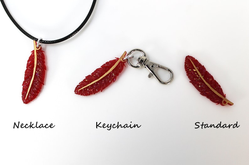 May include: Three red feather charms with gold accents. The feather charms are shown in three different styles: necklace, keychain, and standard.