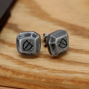May include: A pair of silver stud earrings with a geometric design and a shield symbol engraved on each earring.