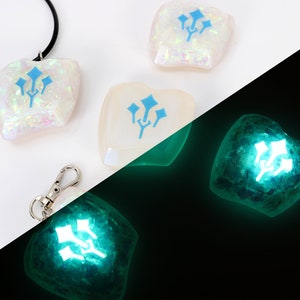 May include: A white, iridescent, resin pendant with a blue three-pronged symbol. The pendant is on a black cord and is also available as a keychain. The pendant glows green in the dark.