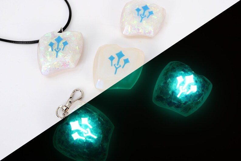 May include: A white, iridescent, resin pendant with a blue three-pronged symbol. The pendant is on a black cord and is also available as a keychain. The pendant glows green in the dark.