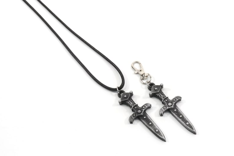 May include: A black leather cord necklace with a silver sword pendant. A matching silver sword keychain is also included.