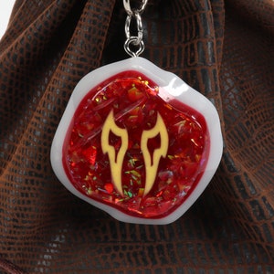 May include: A red and white resin dice bag charm with a gold flame design. The charm is attached to a silver chain.
