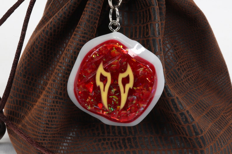 May include: A red and white resin dice bag charm with a gold flame design. The charm is attached to a silver chain.