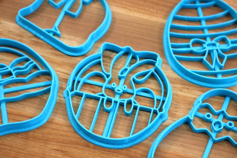 May include: Five blue plastic cookie cutters shaped like Easter eggs, a bunny in an egg, a bunny, and two other shapes.