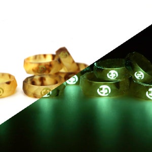 May include: A set of glow-in-the-dark rings with a geometric design and a symbol in the center. The rings are a light brown color in daylight and glow green in the dark.