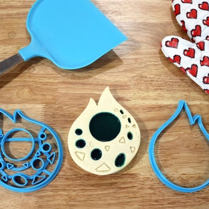 May include: Three blue cookie cutters shaped like flames, one with a circle and smaller shapes inside, and one with a filled-in green circle inside. A yellow cookie with a green circle inside and smaller shapes around it.