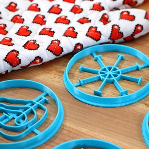 May include: Four blue plastic cookie cutters on a wooden surface. The cutters are shaped like a snowflake, a swirl, a hand, and a pair of scissors.