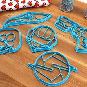 May include: A set of six blue plastic cookie cutters shaped like a spaceship, a helmet, a gun, a claw, a circle with a design inside, and a dinosaur head.