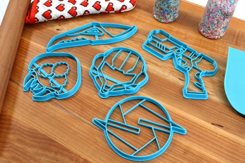 May include: A set of six blue plastic cookie cutters shaped like a spaceship, a helmet, a gun, a claw, a circle with a design inside, and a dinosaur head.